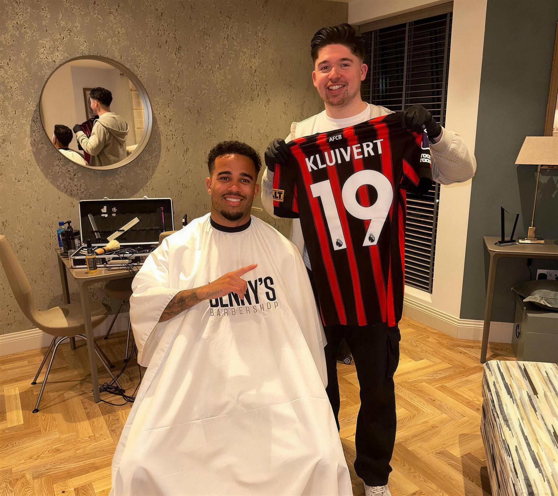 A footballer in the Benny's cape, next to his barber holding up a signed shirt