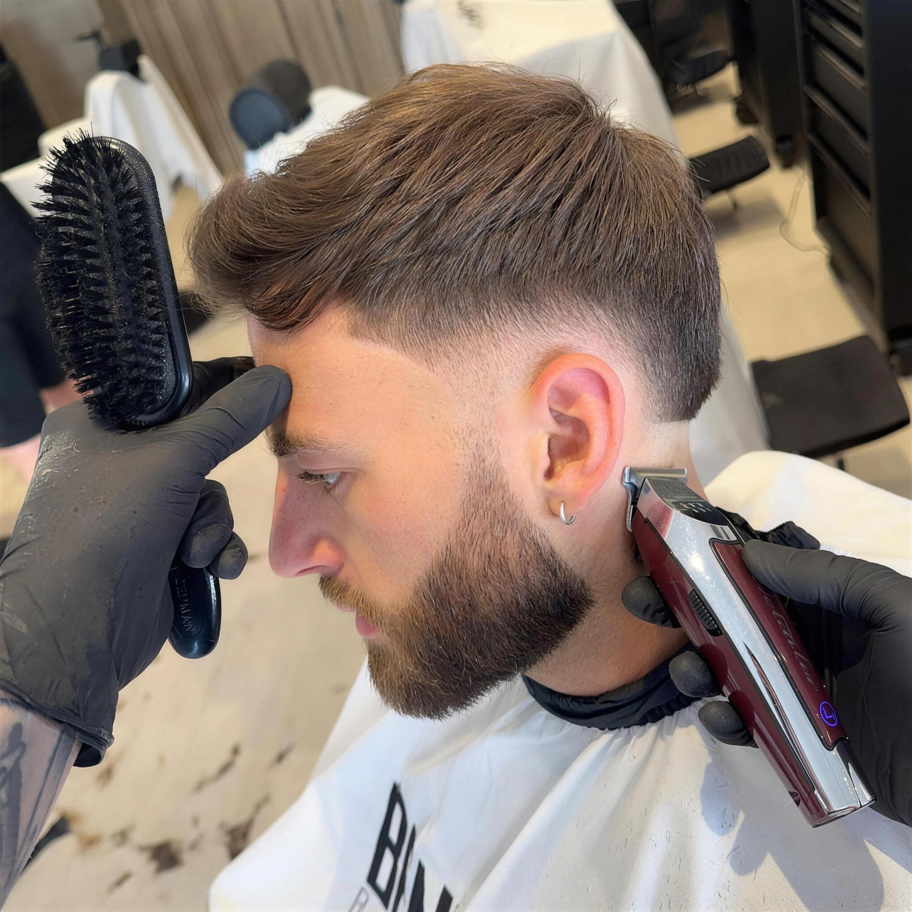 A barber at Benny's tidying a taper on a customer with a full beard