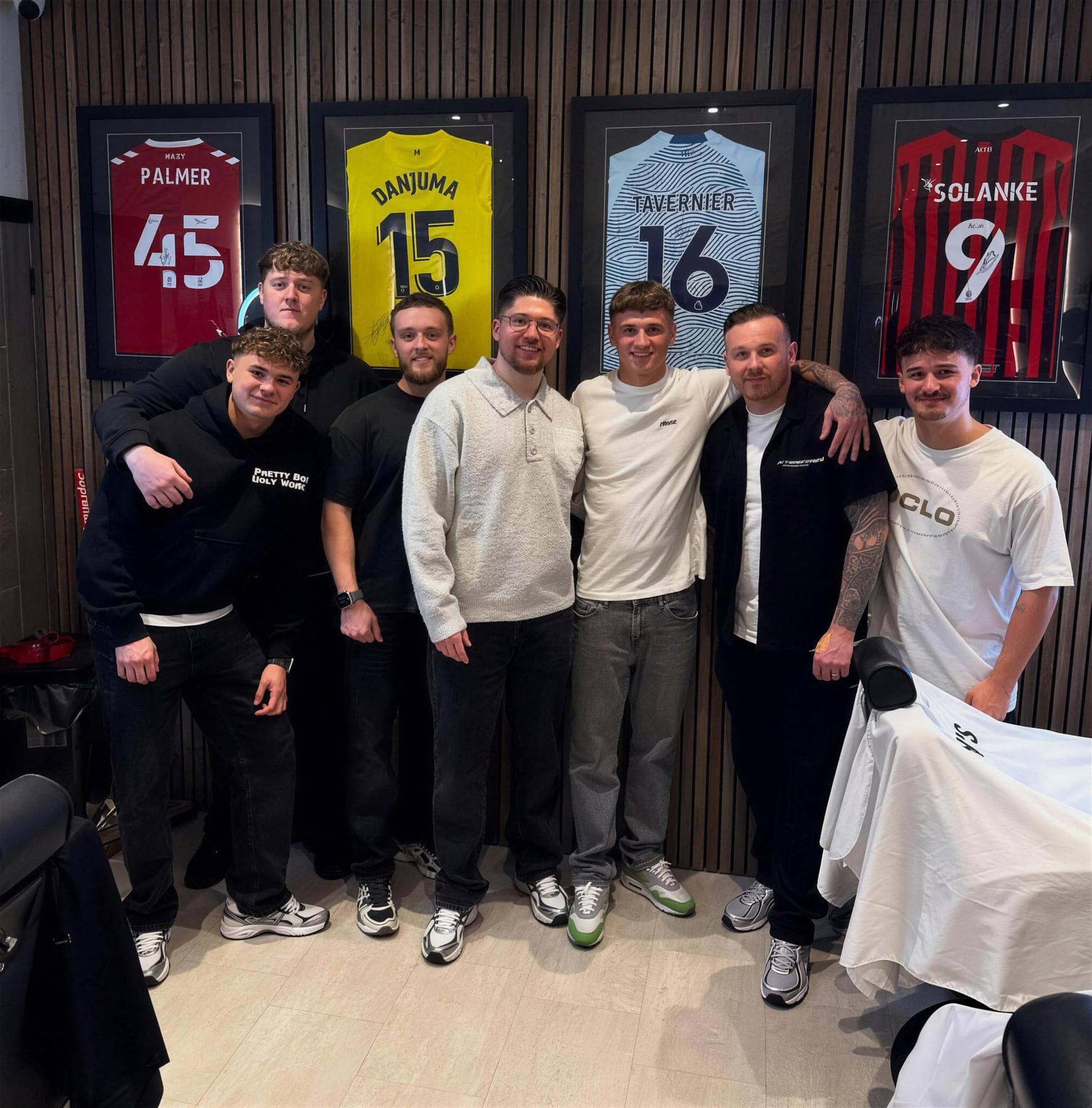 The team at Benny's Barbershop, in front of signed football shirts